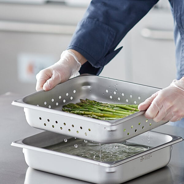 A person in gloves holding a Vigor stainless steel steam table pan of asparagus.