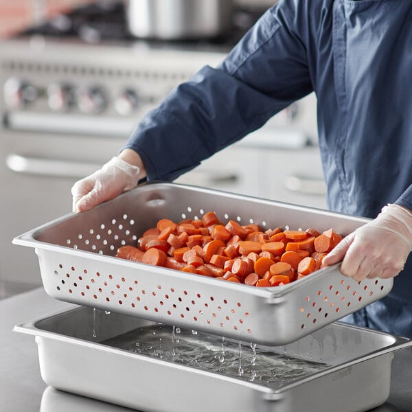 A person in a blue uniform holding a Vigor stainless steel pan full of carrots.
