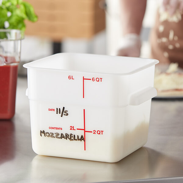 A person measuring white liquid into a Carlisle square white food storage container.