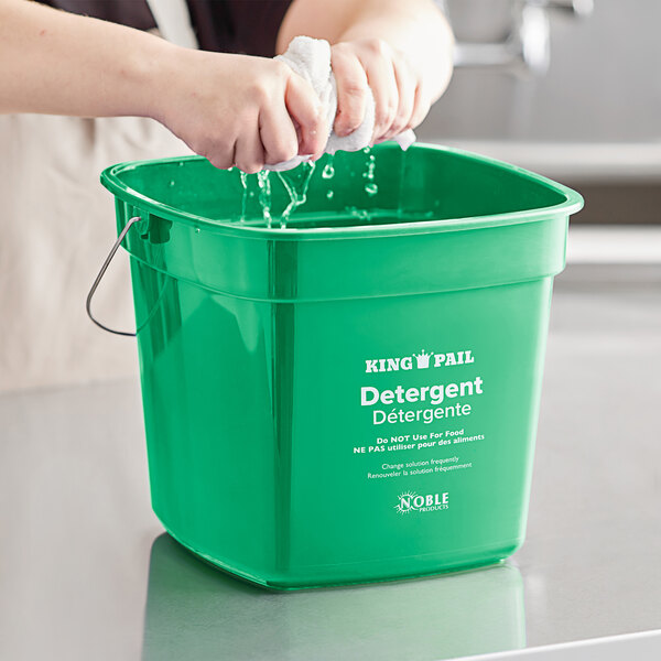 A person washing a green Noble Products King-Pail with detergent.