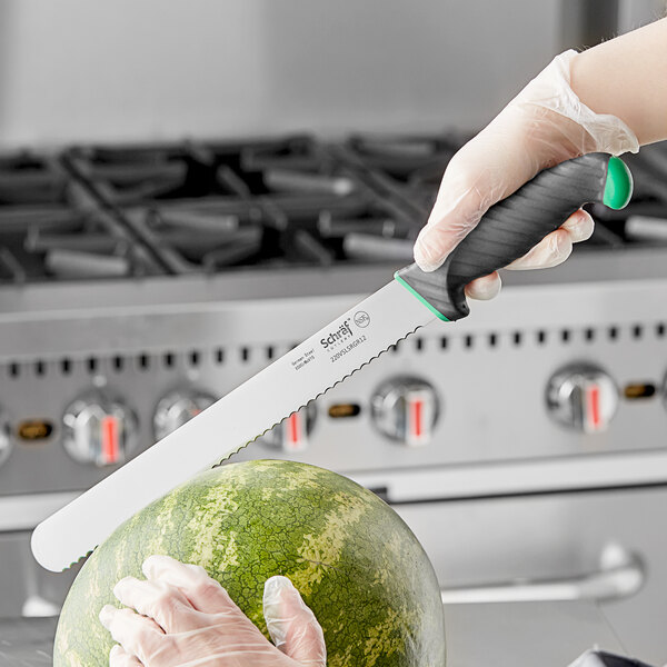 A person using a Schraf serrated slicing knife with a green handle to slice a watermelon.