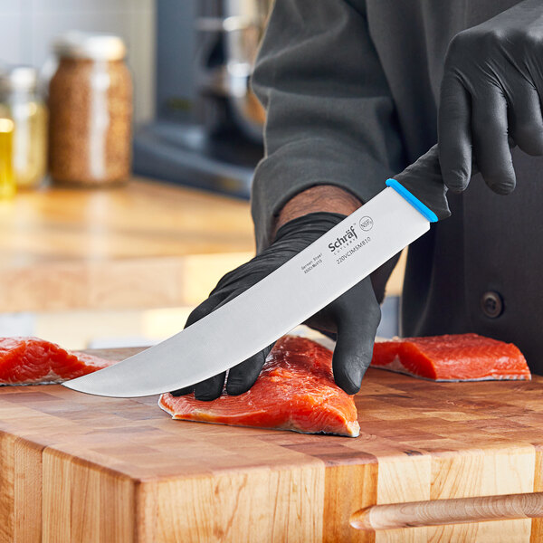 A person in black gloves using a Schraf Cimeter knife to cut meat on a cutting board.