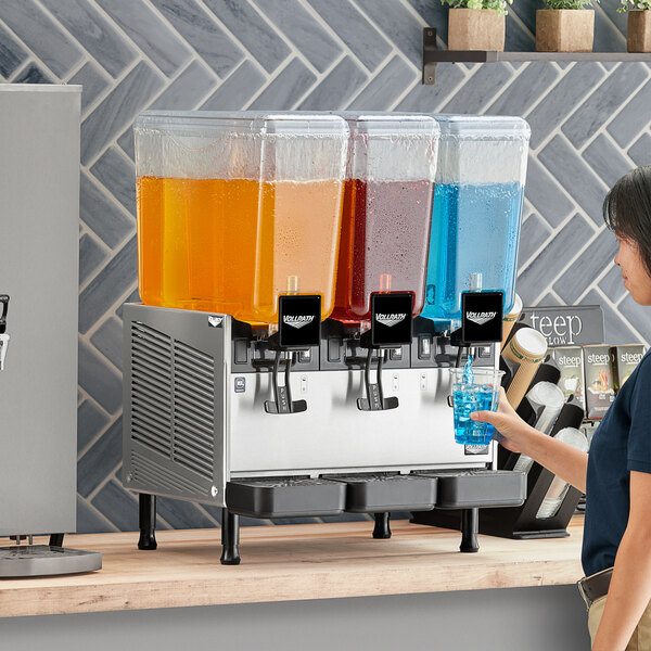A woman pouring blue liquid into a Vollrath refrigerated beverage dispenser.