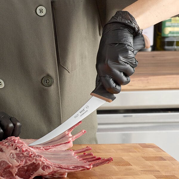 A person wearing a black glove cutting raw meat with a Schraf curved boning knife.
