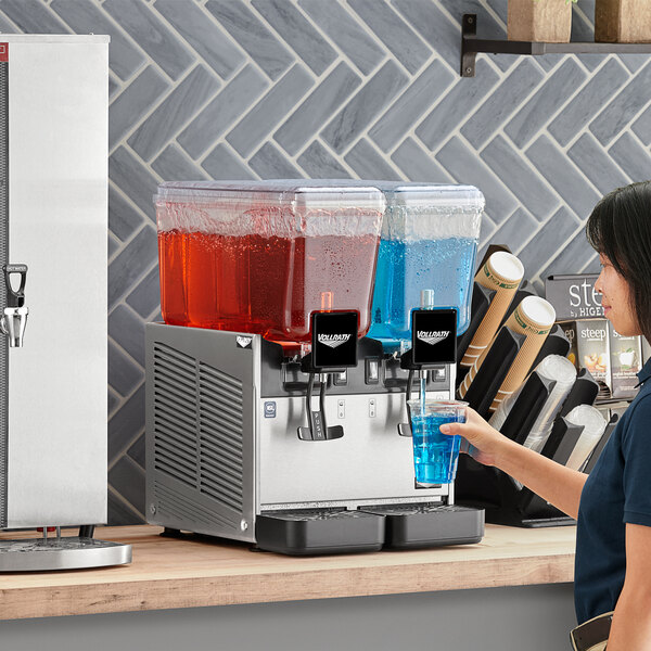 A woman using a Vollrath refrigerated beverage dispenser to pour a blue drink.