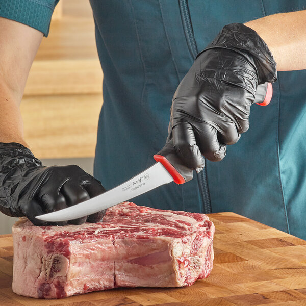 A person in a black glove using a Schraf curved boning knife to cut up meat.