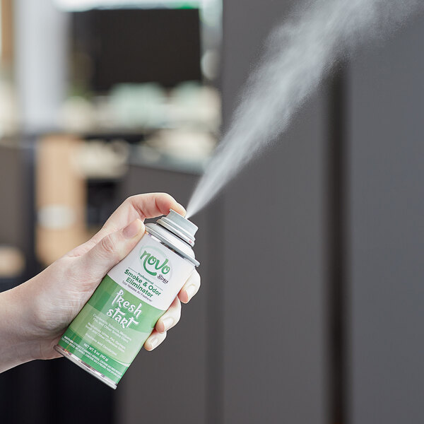 A hand holding a Novo by Noble Chemical Fresh Start Total Release air freshener can spraying in a room.