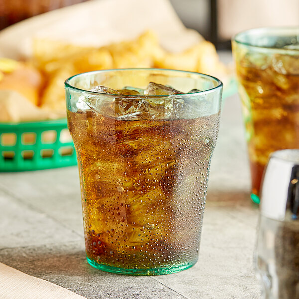 A green Choice plastic tumbler filled with ice tea on a table.