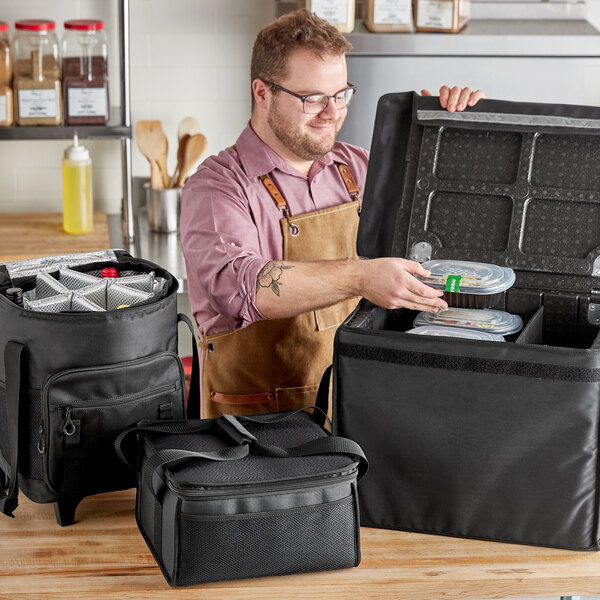 A man in an apron opening a black ServIt cooler bag with wheels.