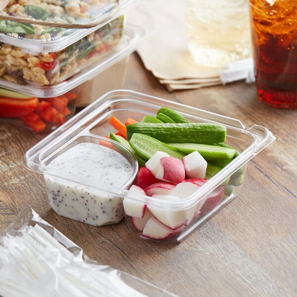 A Dart TamperGuard plastic container with salad, vegetables, and dip on a table.