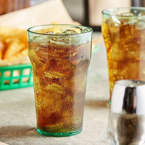 Two Choice green plastic tumblers filled with ice tea on a table with a basket of chips.