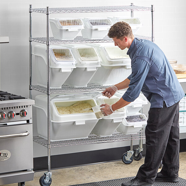 A man using a Baker's Mark ingredient bin shelving kit to store food in white containers with clear lids.