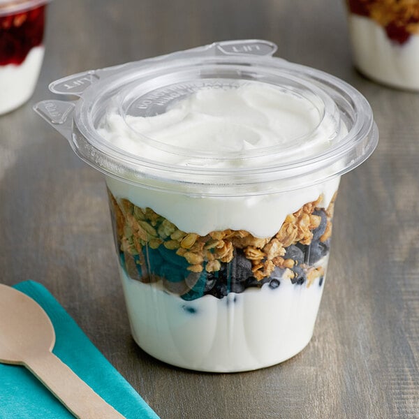 A Dart plastic cup filled with yogurt and granola with a wooden spoon on a napkin.