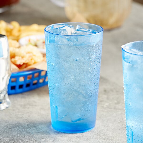 Two blue Choice plastic tumblers filled with ice on a table with a blue basket of fries.