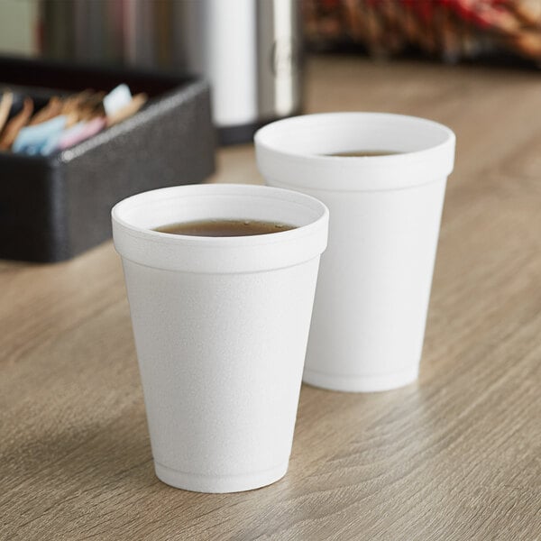 Two Dart white foam cups with brown liquid on a table.