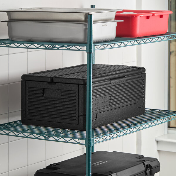 A black insulated food pan carrier with two full-size food pans and lids, placed on a wire shelving unit.