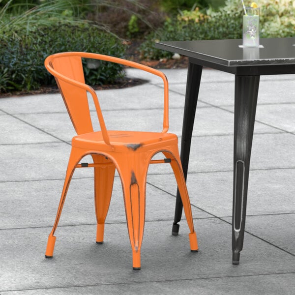 A Lancaster Table & Seating distressed orange arm chair on a patio next to a table.