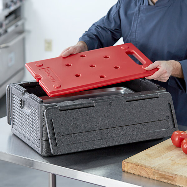 A man putting a red plastic board into a black CaterGator Dash food pan carrier.