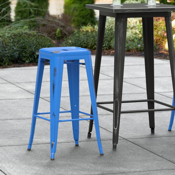 Two Lancaster Table & Seating distressed blue metal barstools on an outdoor patio.