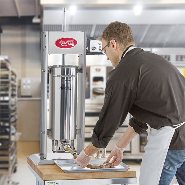A man using an Avantco stainless steel sausage stuffer in a commercial kitchen.