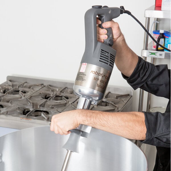 A person using a Robot Coupe immersion blender with a whisk attachment to mix a large bowl.