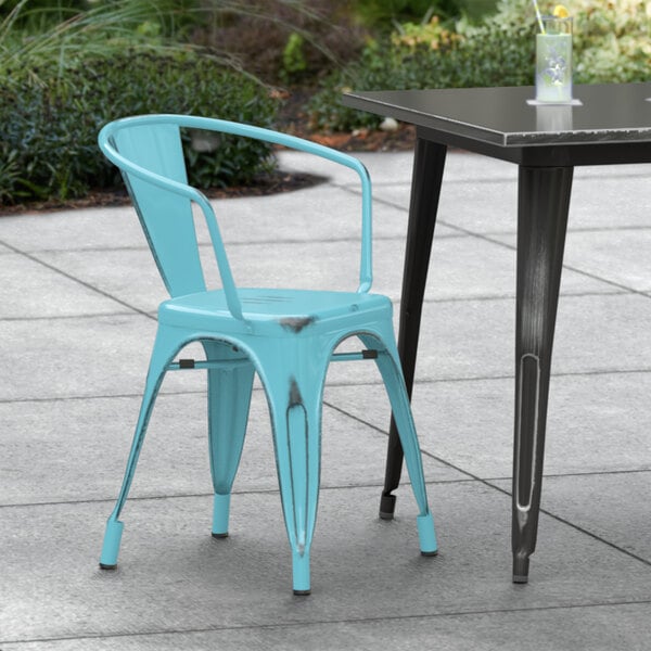 A Lancaster Table & Seating distressed arctic blue metal arm chair on a concrete patio next to a table.