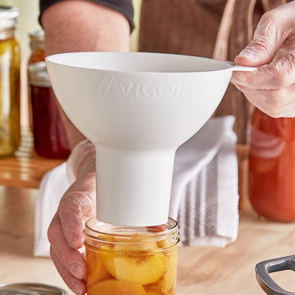 A person using a white Vigor wide mouth canning funnel to pour peaches into a jar.