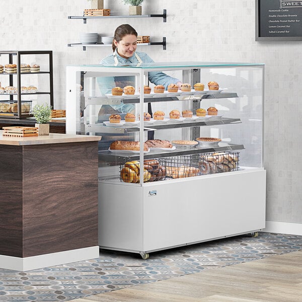 A woman standing behind a white Avantco dry bakery display case with pastries.