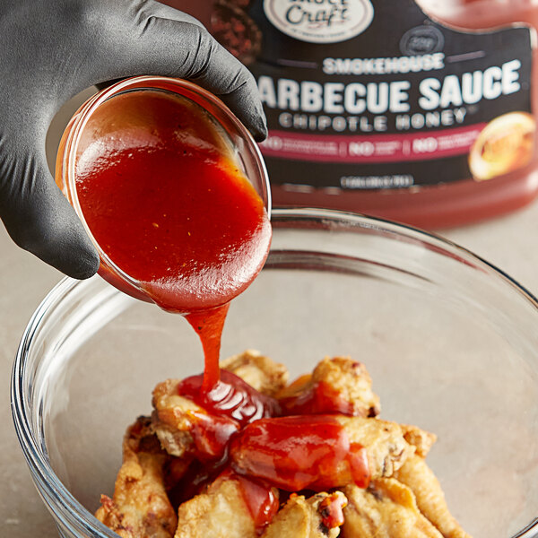 A person pouring Sauce Craft Chipotle Honey BBQ sauce into a bowl of chicken.