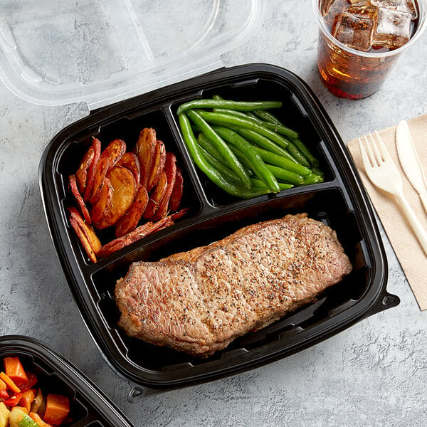 A black plastic hinged container with steak, vegetables, and a drink inside.