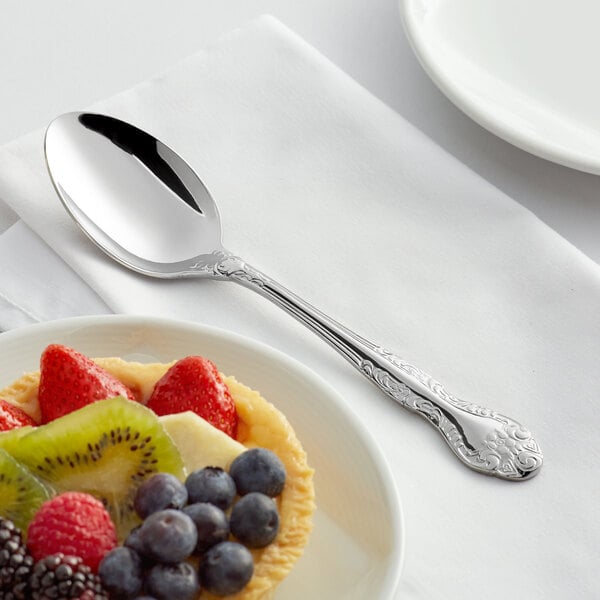 An Acopa Capulet stainless steel dinner spoon on a napkin next to a plate of fruit.