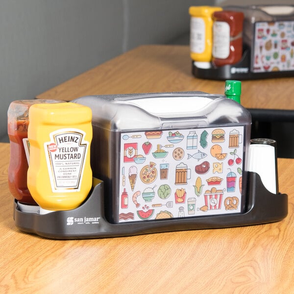 A San Jamar Venue tabletop napkin dispenser with condiments on the table.