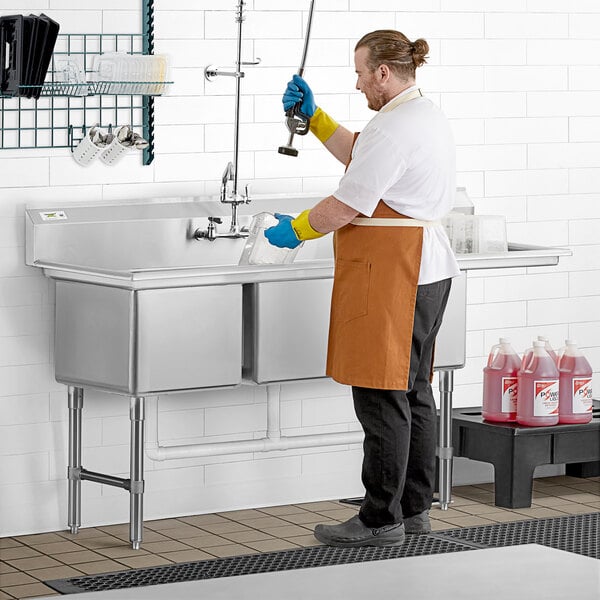 A man in an apron washing a Regency 3 compartment commercial sink on a counter in a professional kitchen.