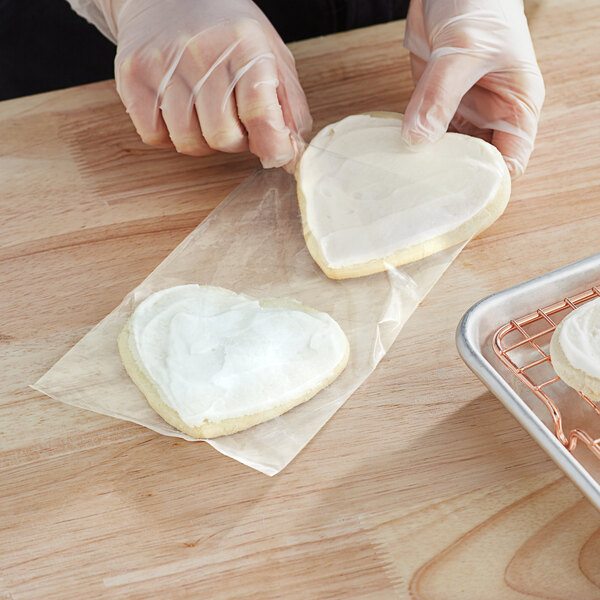 A person wearing plastic gloves frosting a heart shaped cookie.