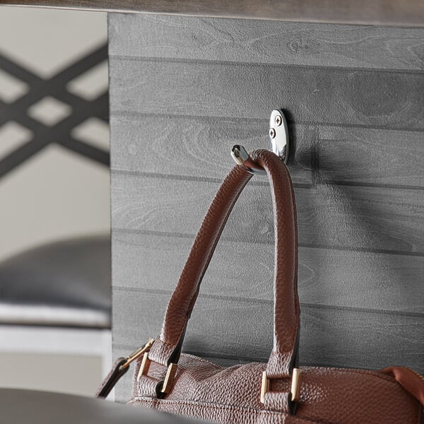 A brown purse hanging on a Lancaster Table & Seating chrome bar purse hook on a restaurant table.