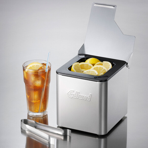 An Edlund stainless steel condiment holder with a black insert next to a glass of ice tea with lemons in it.