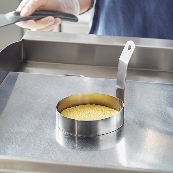 A person using a Choice stainless steel egg ring in a pan with eggs.