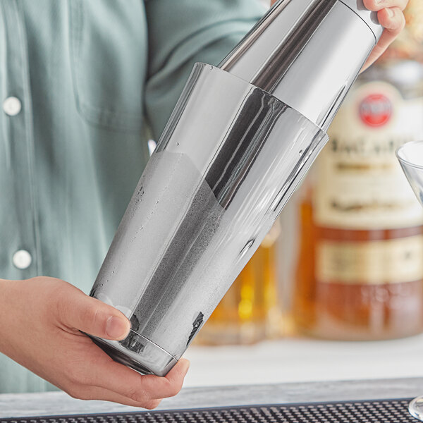 A person using an Acopa stainless steel cocktail shaker to make a drink.