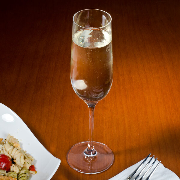 A Stolzle flute glass filled with wine on a table next to a plate of pasta.