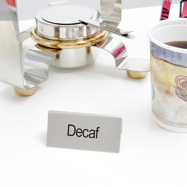 A stainless steel double sided "Decaf" table tent on a table with a cup of coffee.