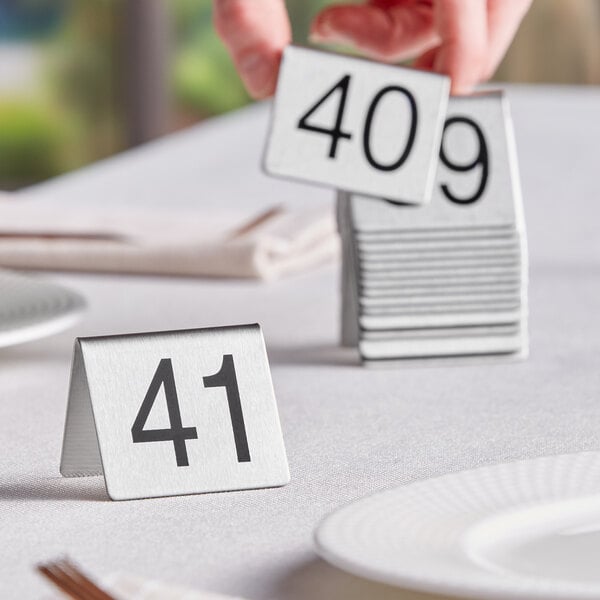 A hand holding a white square with black numbers on a table.