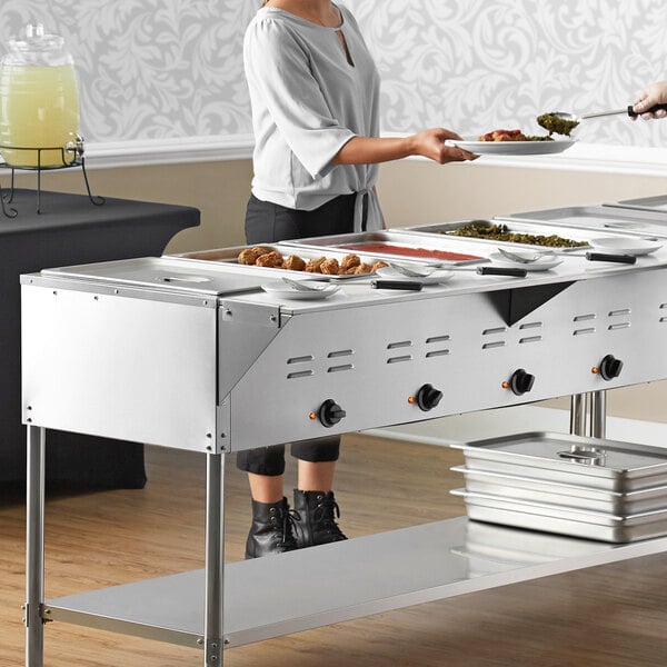 A woman serving food at a buffet using an Avantco mobile electric steam table.