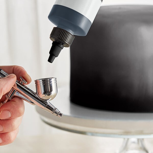 A person holding a silver airbrush spraying a cake black.
