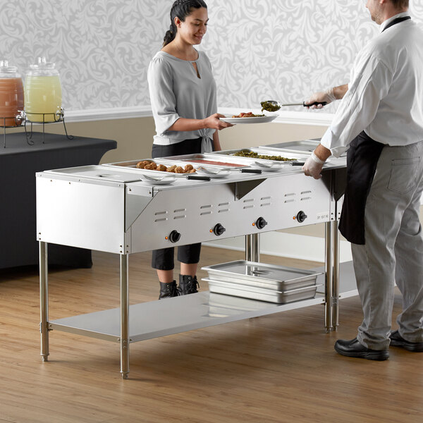 A man and woman standing next to an Avantco electric steam table.