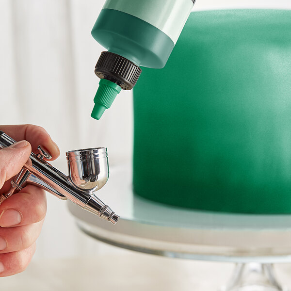 A person holding a Chefmaster Metallic Green airbrush color bottle.