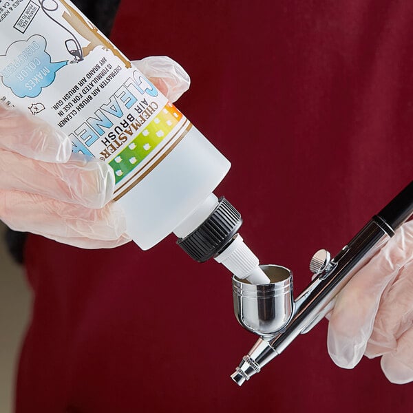 A gloved hand using Chefmaster Airbrush Cleaner to clean a spray gun.
