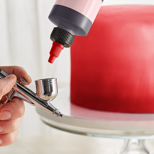 A finger holding a bottle of Chefmaster Flamingo Red airbrush color.