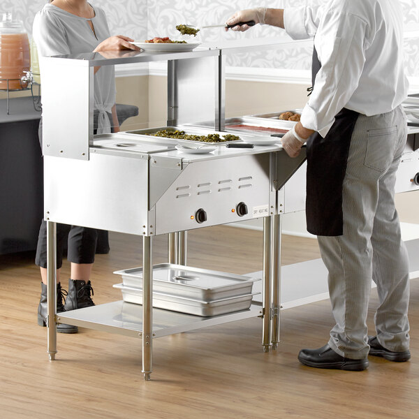 A man serving food from an Avantco electric steam table to a woman on a white counter.