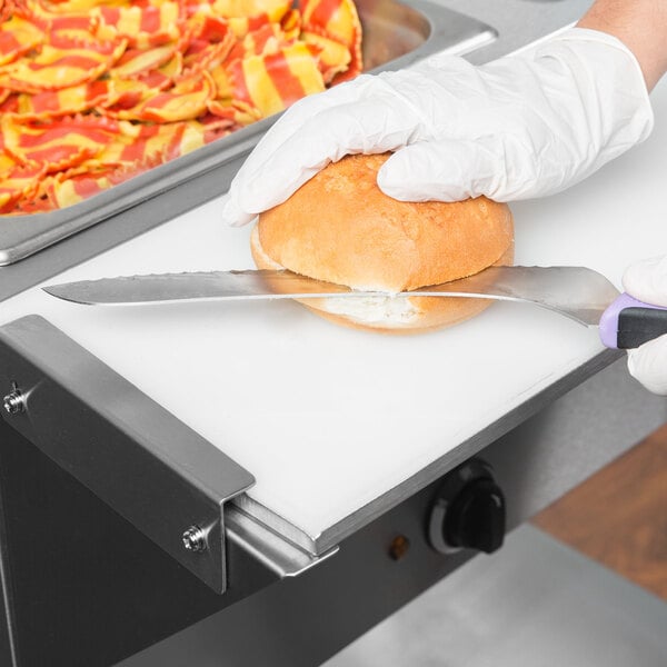 A person in gloves cutting bread on an Avantco cutting board with a knife.
