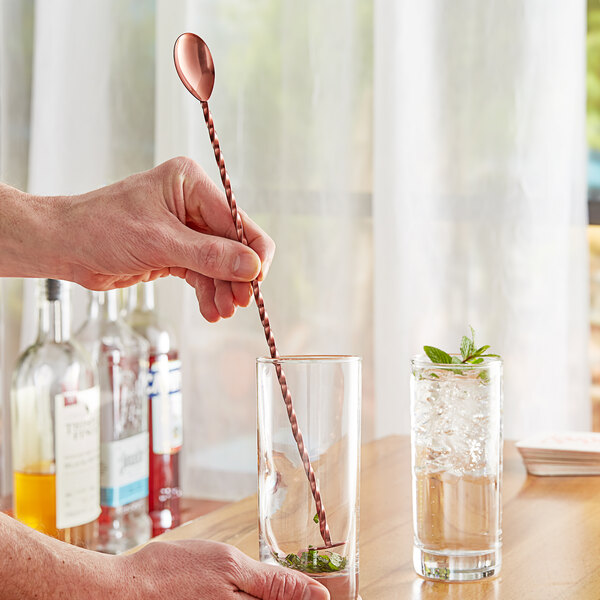 A person using an Acopa copper bar spoon to mix a drink.